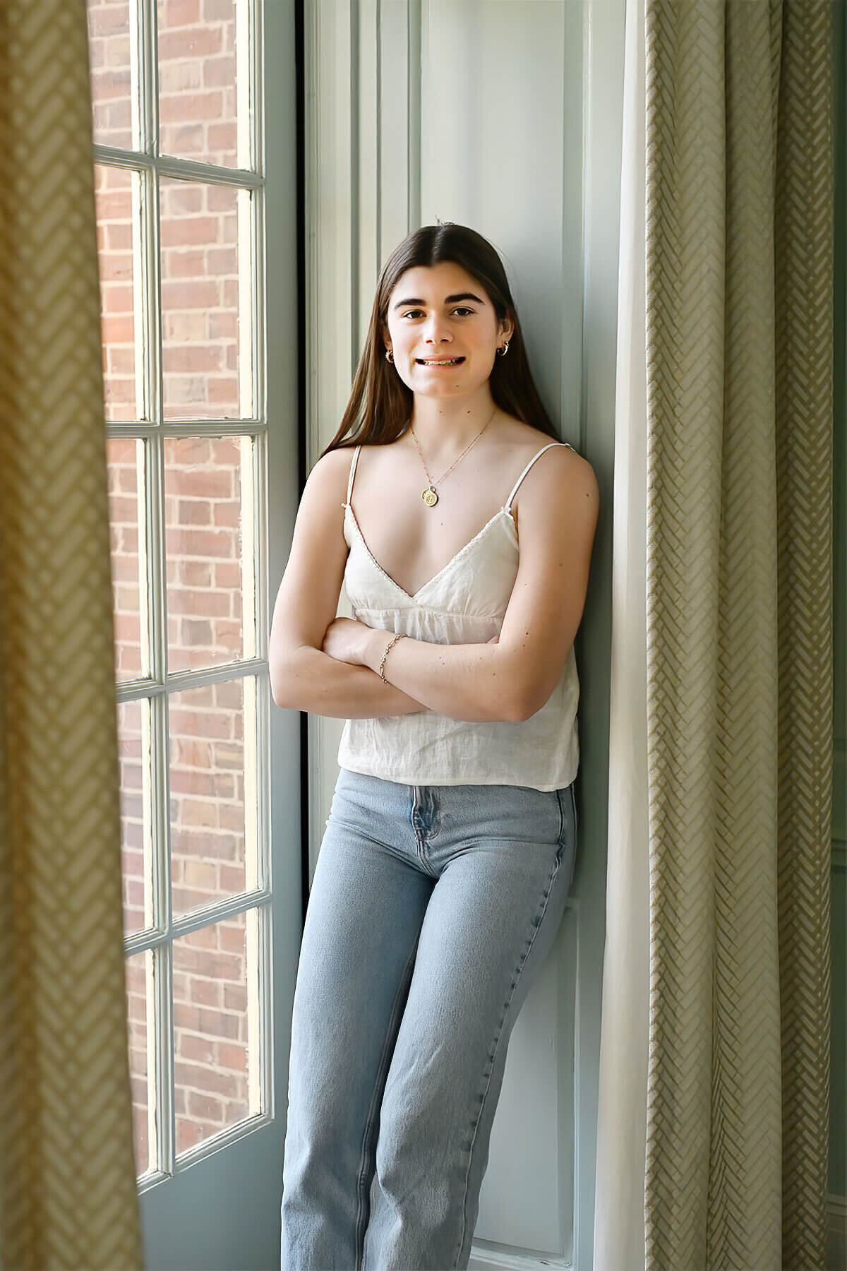 A senior girl leans next to a giant window at the Andover Inn with her arms folded.