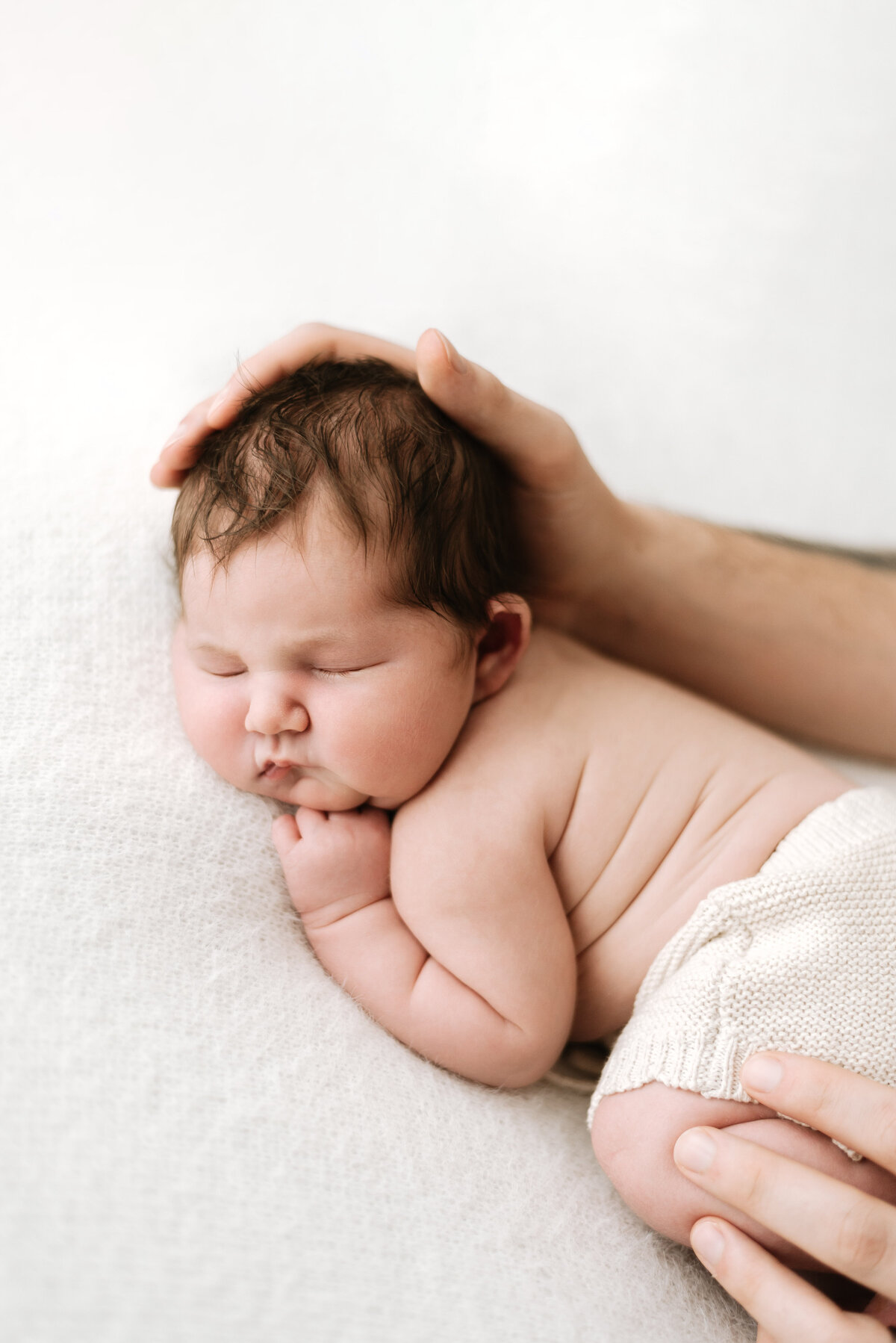 Dad holding baby girl head on white blanket at newborn photoshoot in Billingshurst