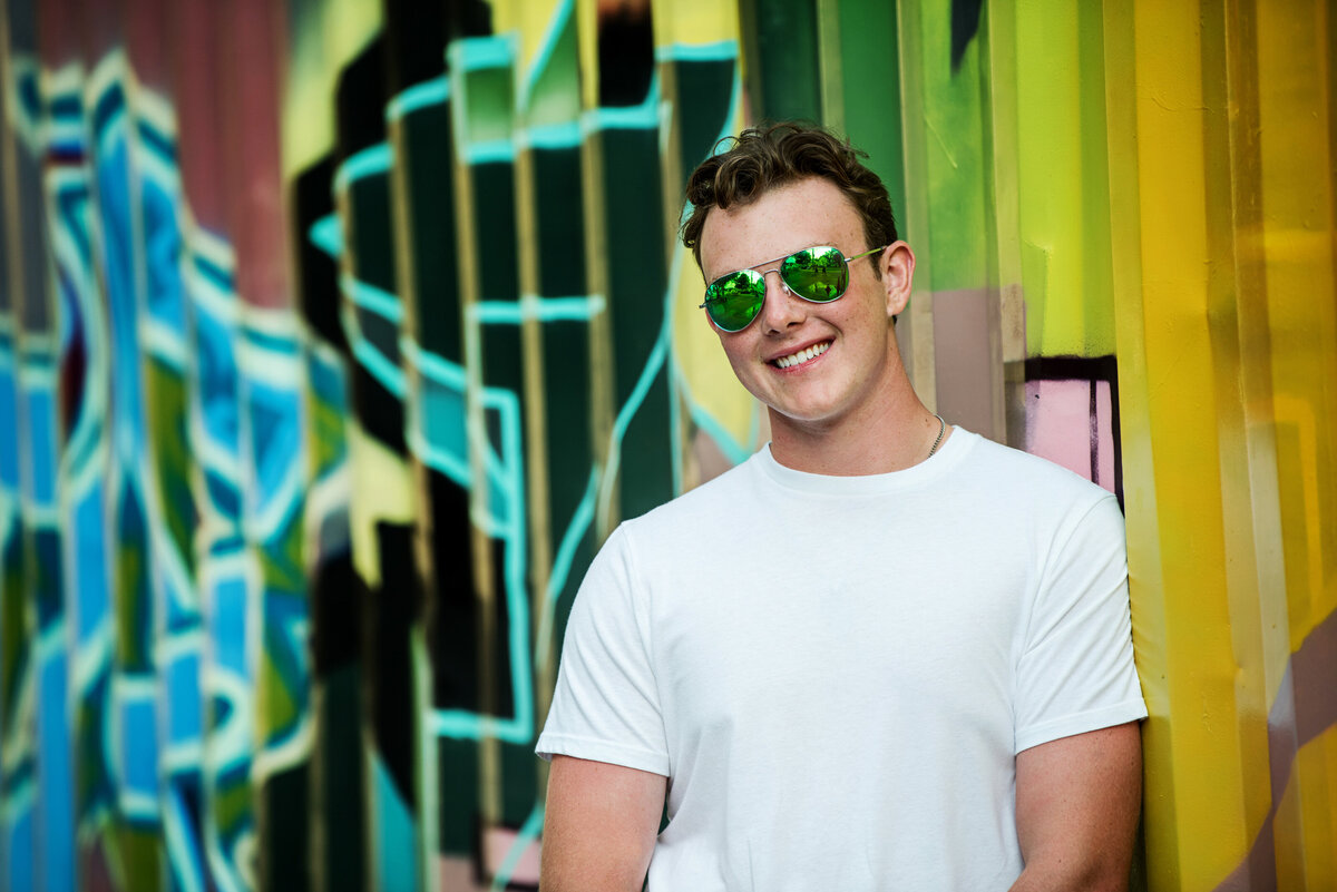 L.A. Senior photo of guy in white shirt and sunglasses against urban mural