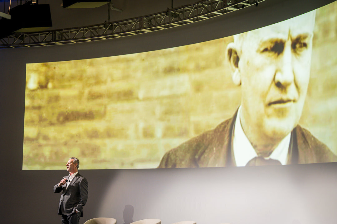 Corporate event photography of speaker presenting to large audience with branded screen backdrop new jersey.