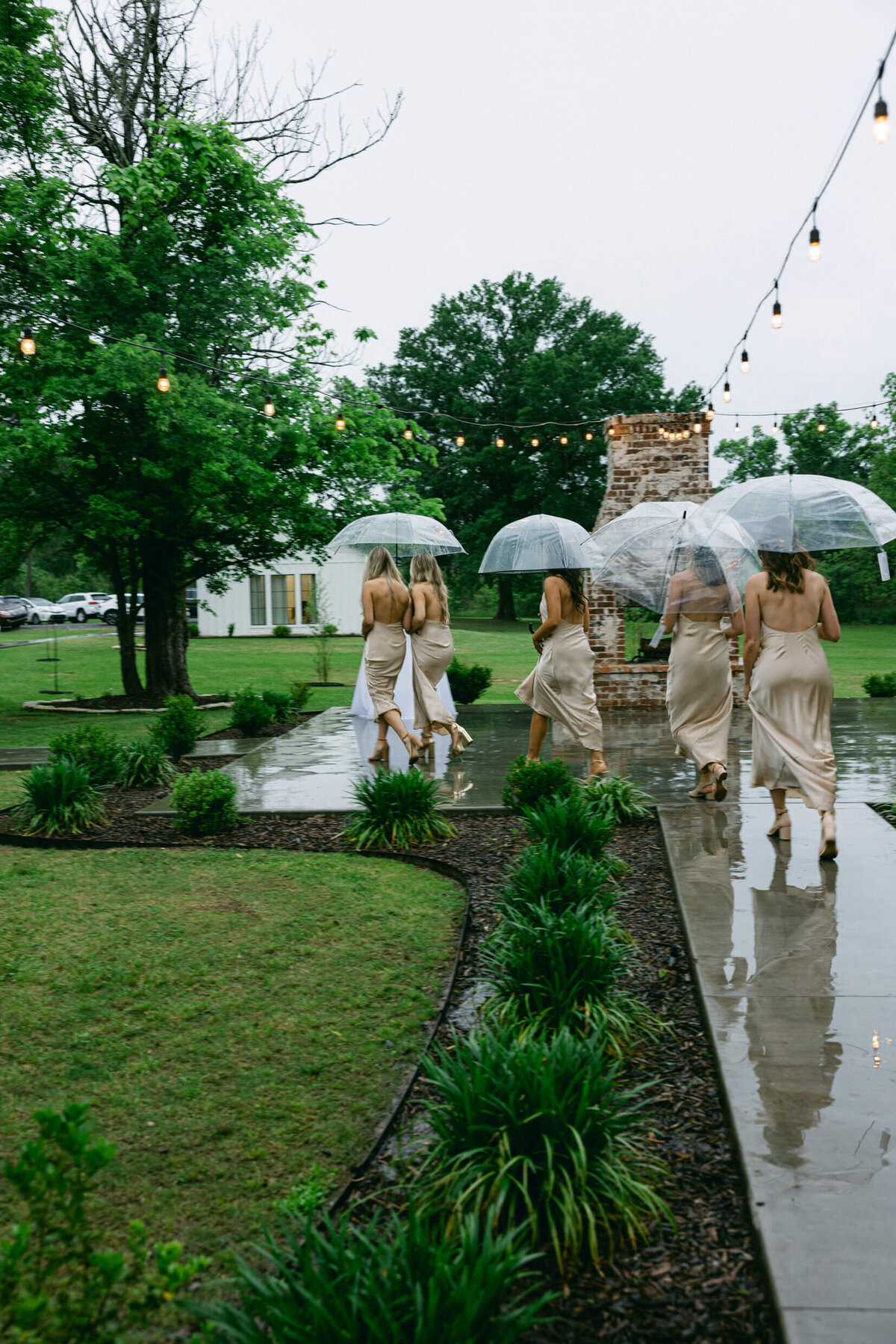 A wedding  photo of the bridesmiads walking to the ceremony holding umbrellas as it is raining