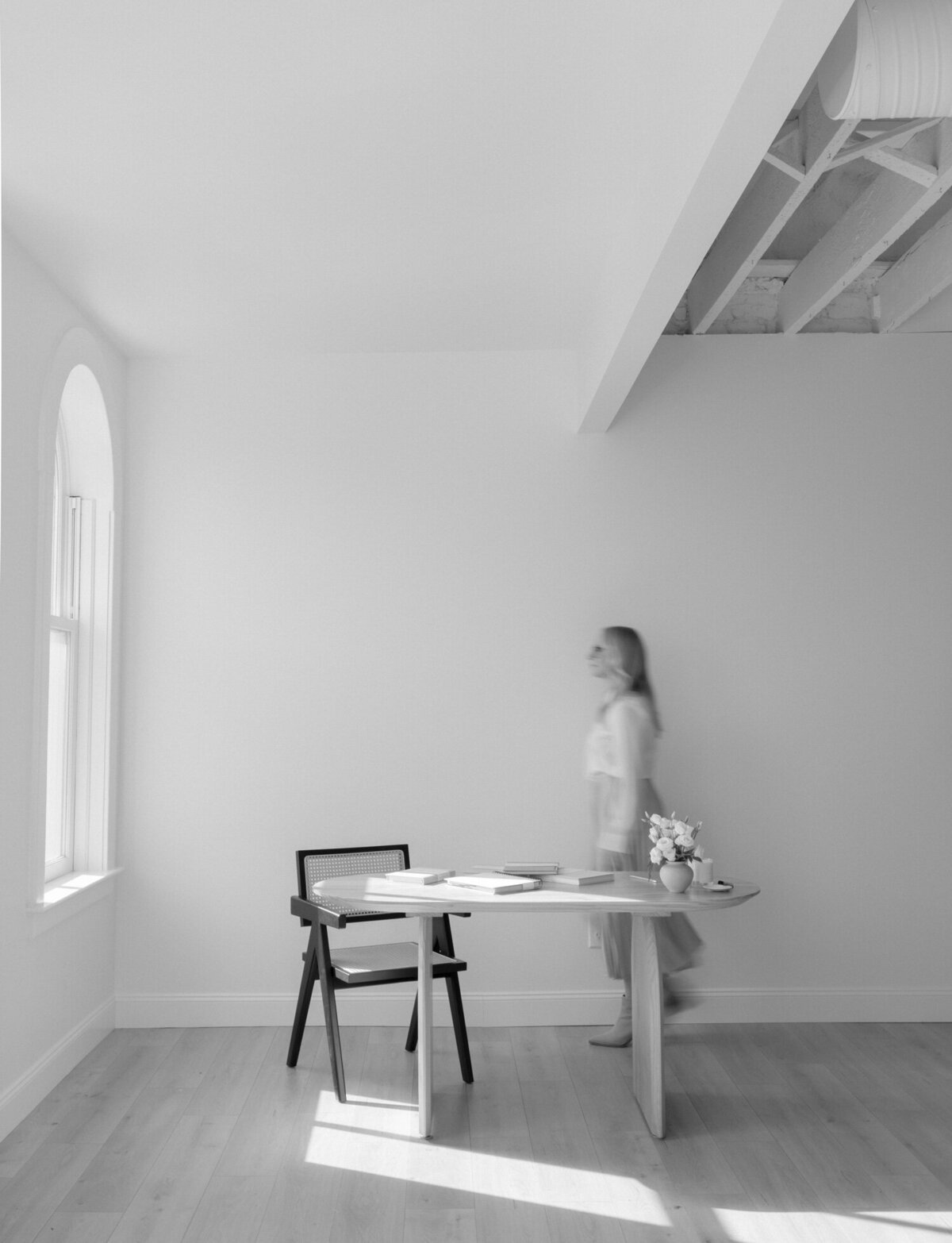 woman in pleated skirt walking behind desk, movement branding photo, white natural light studio