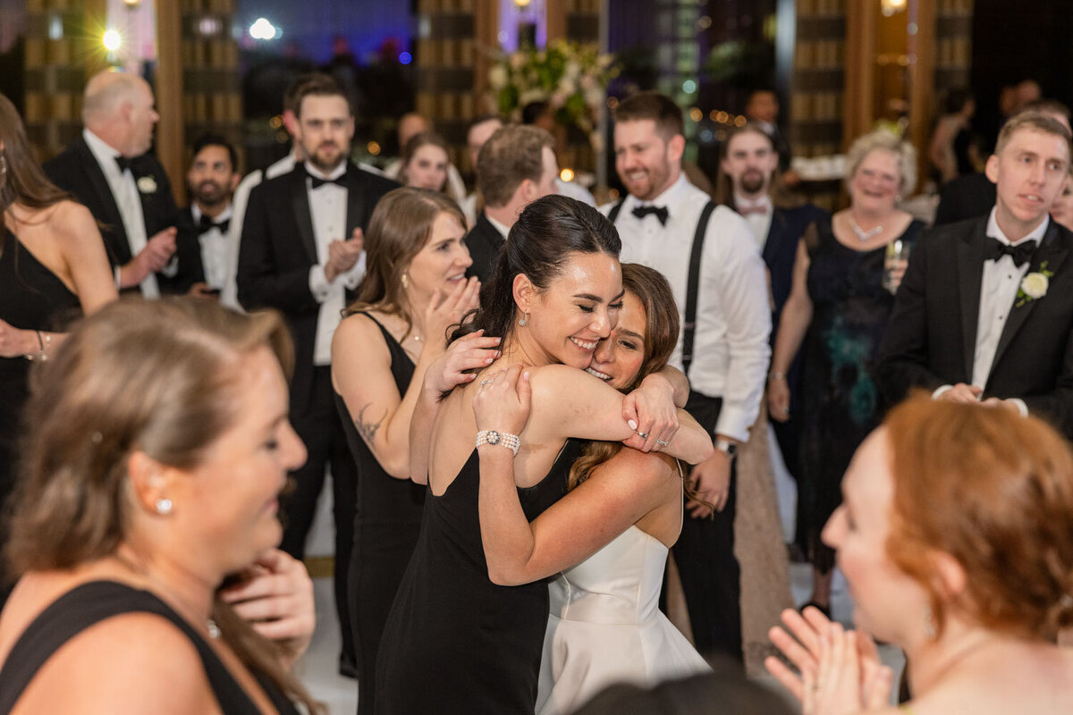 A woman in a white dress is hugging another woman in a black dress.