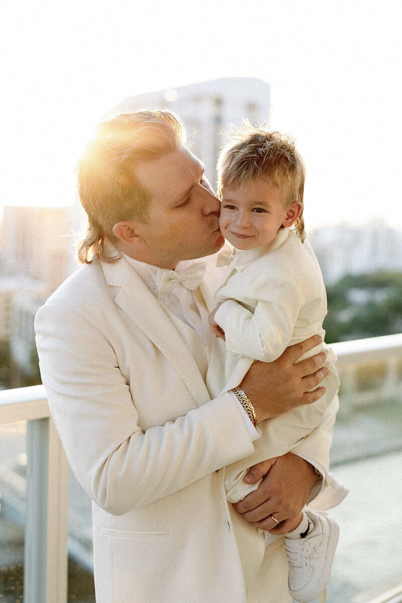 groom kissing son on balcony at the penthouse at riverside wharf​