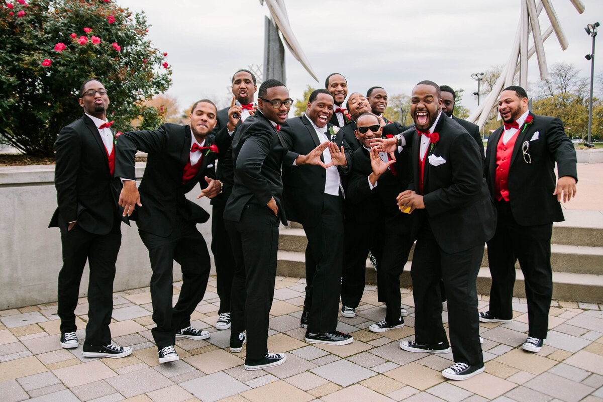 Groom and his groomsmen celebrating the wedding day in black suits with red vests and bow ties.