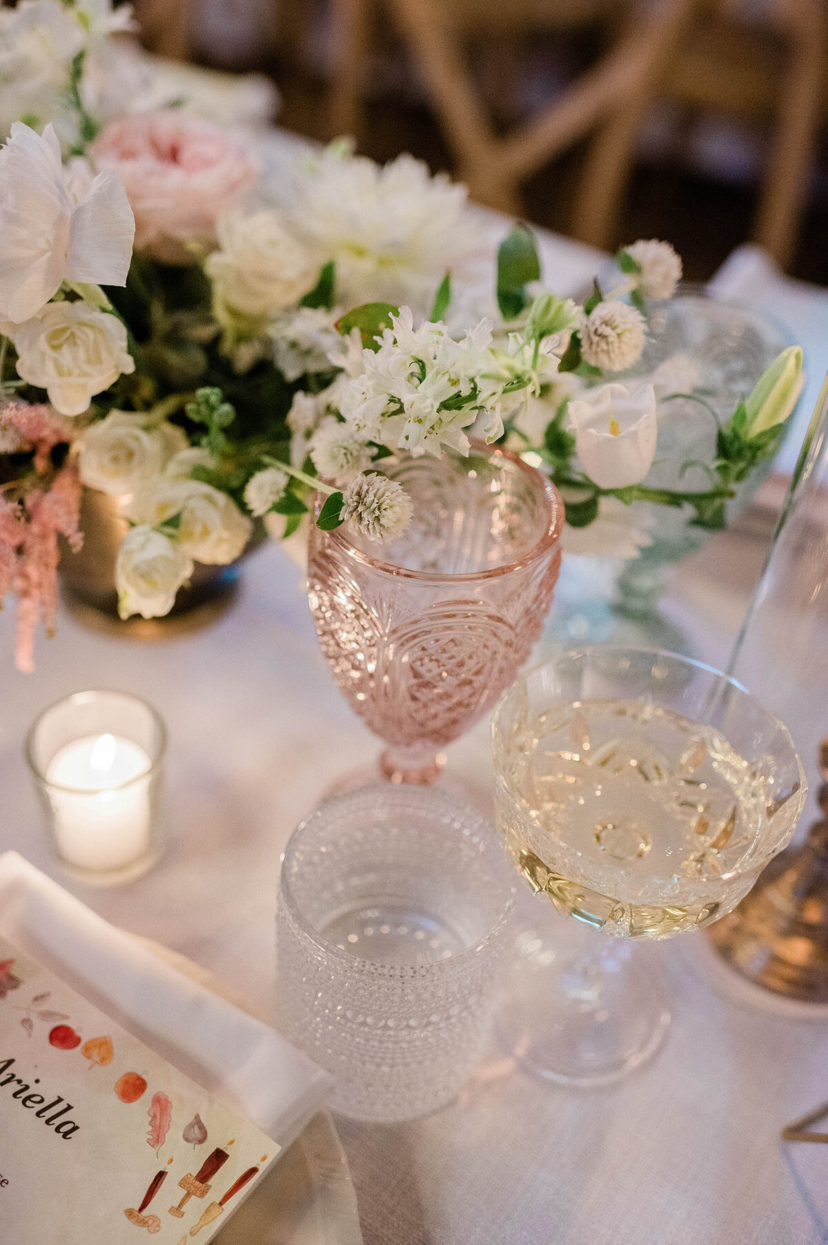 Delicate pink and clear vintage glassware sit beside fresh floral arrangements and candlelight on the wedding table.