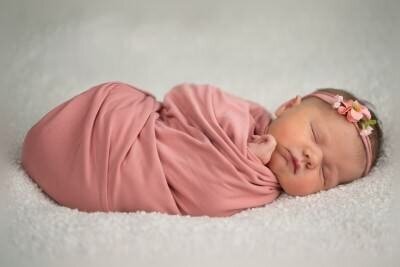 Beautiful newborn baby girl in pink wrap with floral headband by St Augustine newborn photographers on soft white blanket