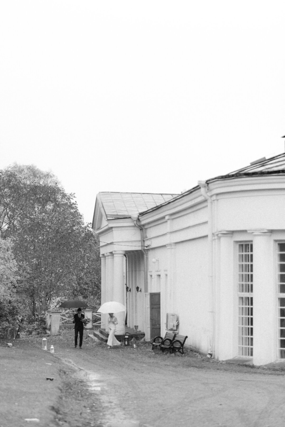 A documentary photograph of a wedding couple coming out of the orangerie with umberellas in Oitbacka gård captured by wedding photographer Hannika Gabrielsson in Finland