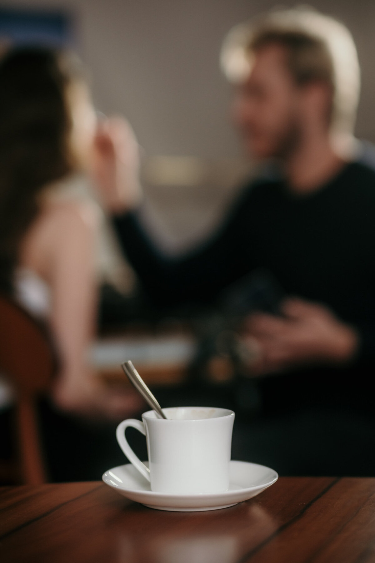 Eine Kaffeetasse ist im Vordergrund fokussiert, während dahinter der Stylist das Model schminkt.