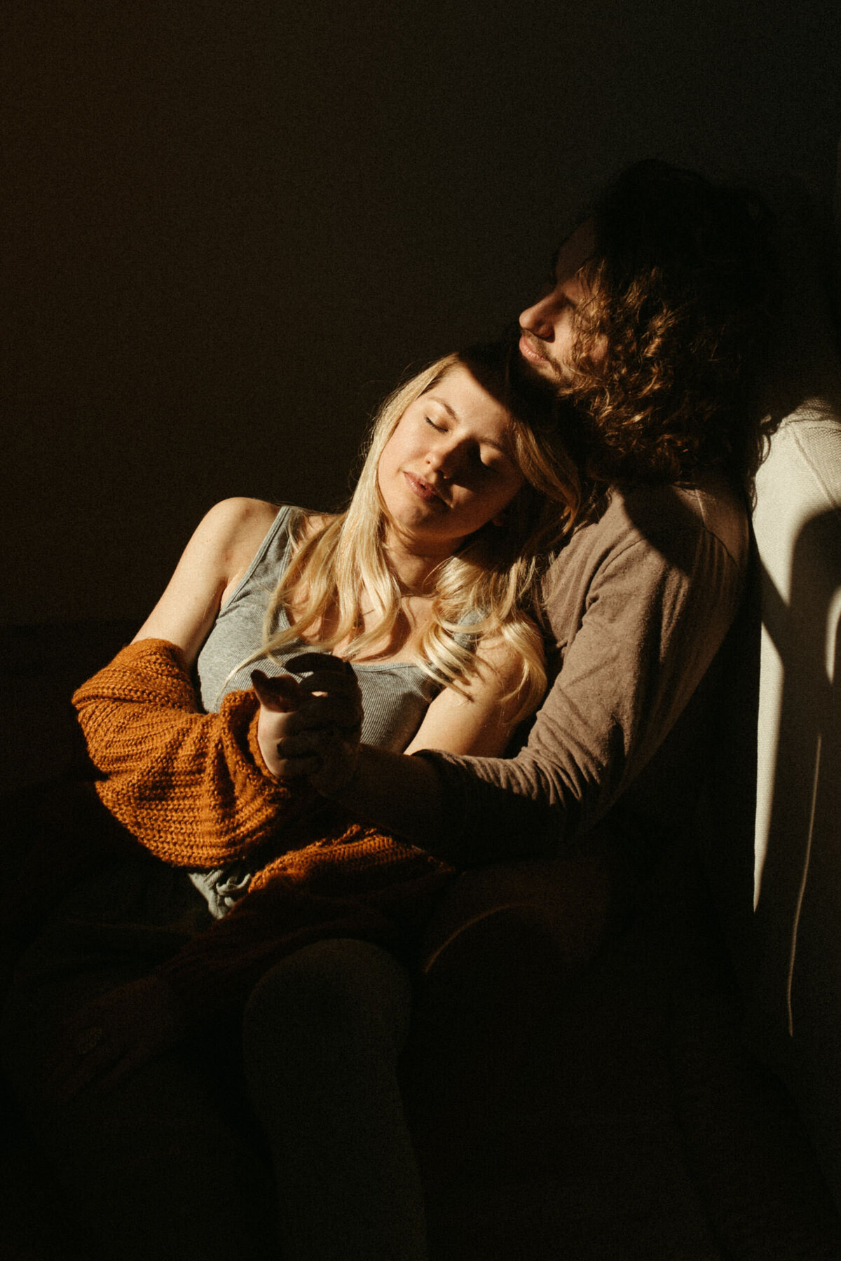 Girl leaning against guy next to a couch inside their home with dramatic lighting