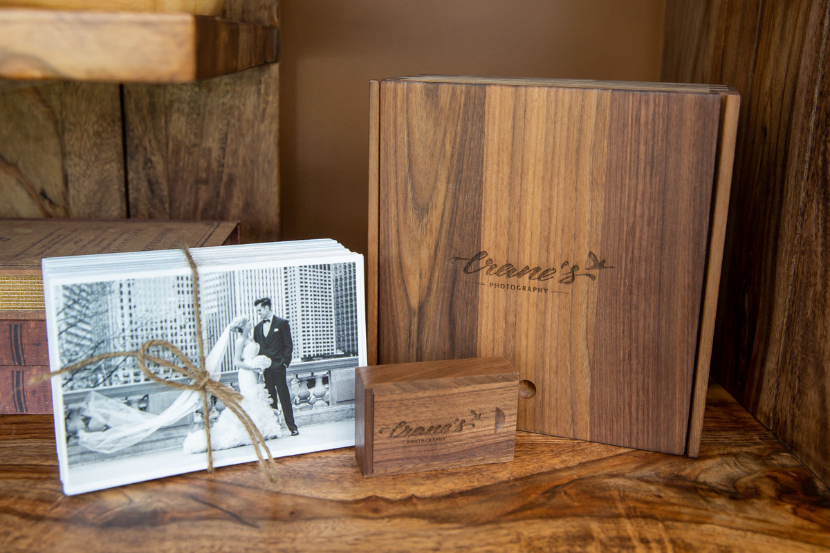 Wooden keepsake wedding box on a shelf next to fine-art prints and USB drive.