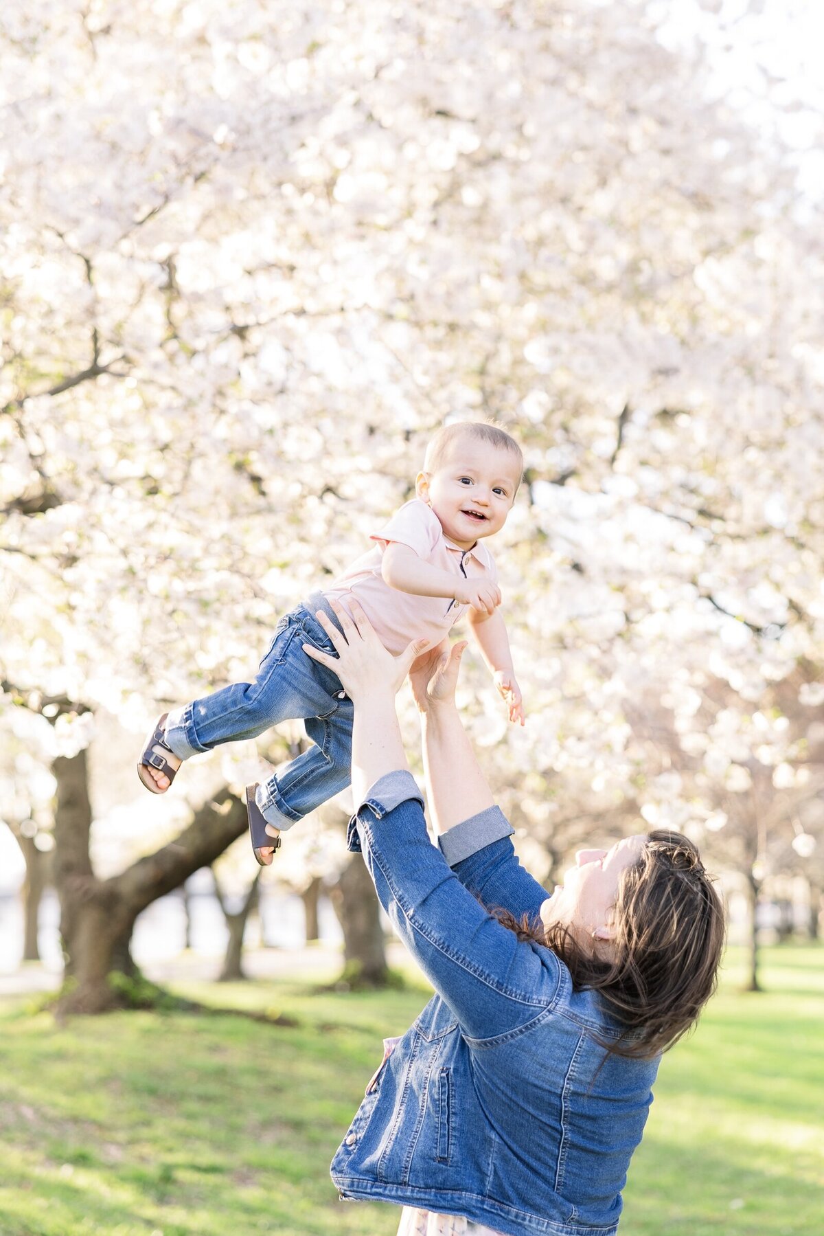 Mom tossing her baby boy in the air amidst the cherry blossoms