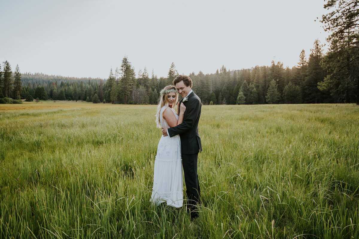 Bride and groom embrace tightly in the middle of wide open forest meadow.