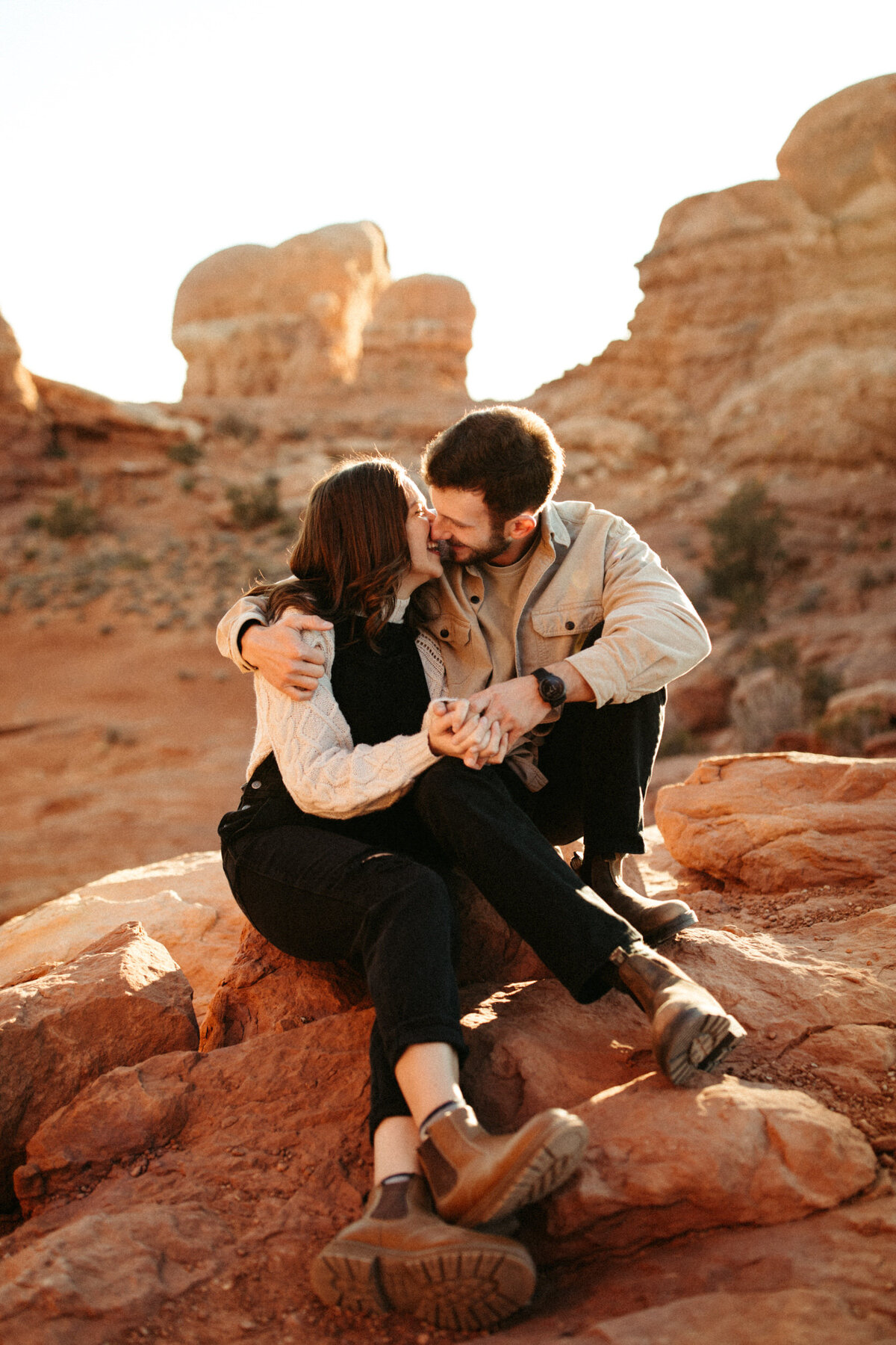 Giggly couple about to kiss while sitting on the red rocks in Arches National Park in Moab, Utah