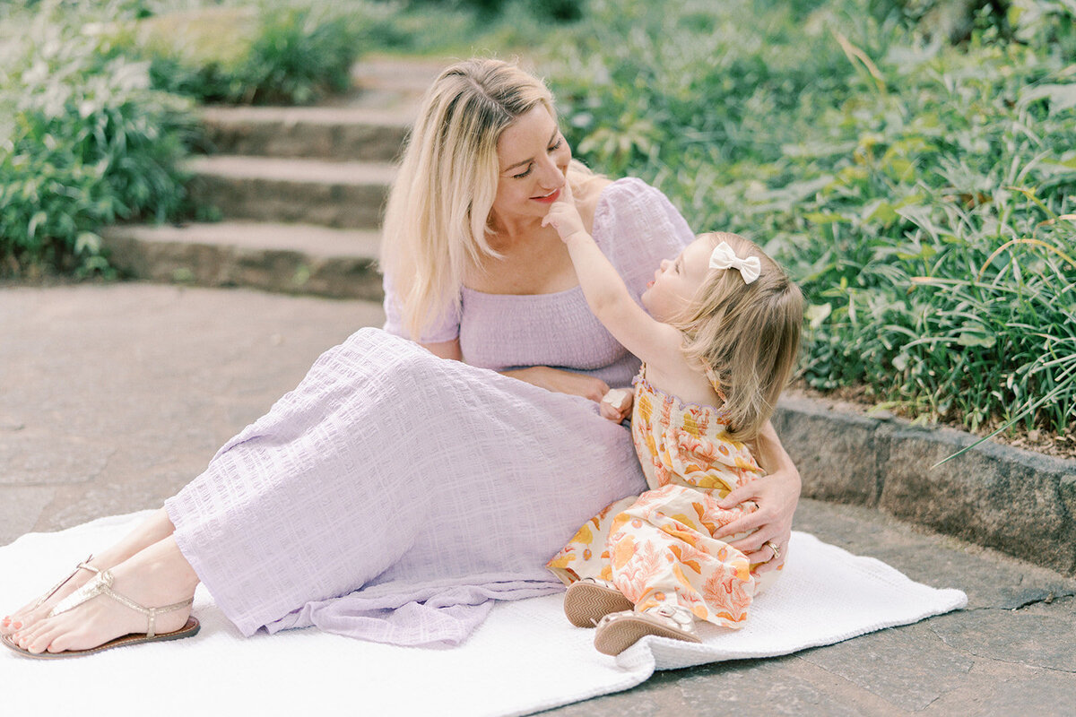 little girl pointing to moms nose while sitting on blanket in park