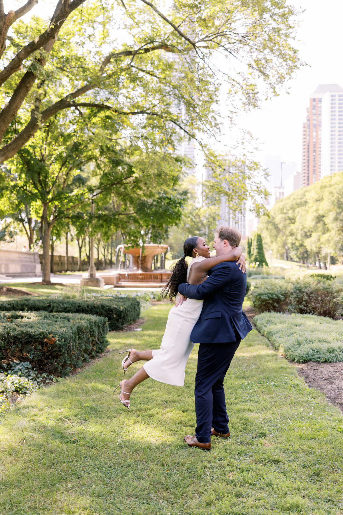 A couple shares a romantic moment in a formal garden along Michigan Avenue, surrounded by lush greenery and city charm.
