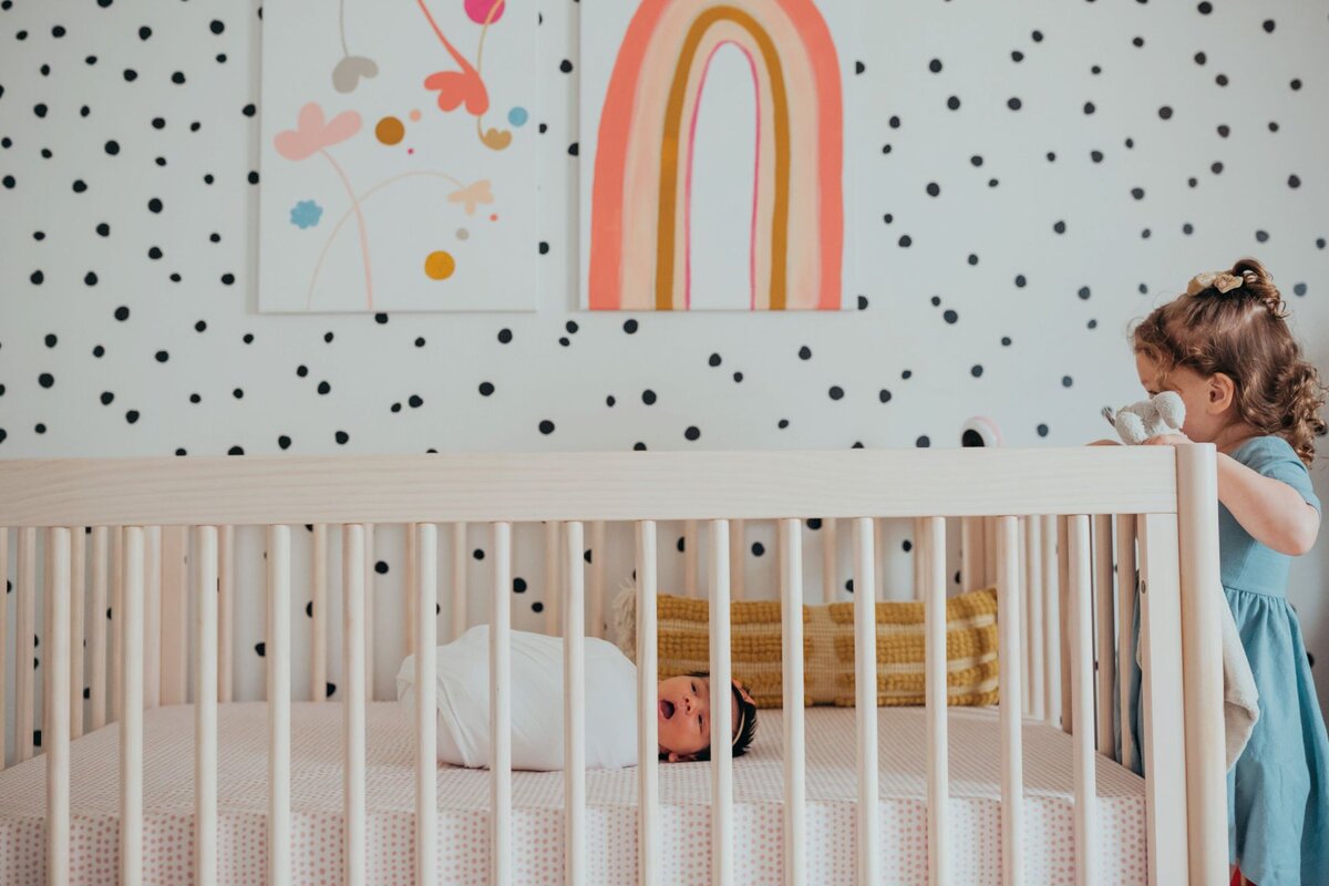 newborn big sister toddler peeking in crib of newborn sister in girl nursery by Orange County photographer Francesca Marchese