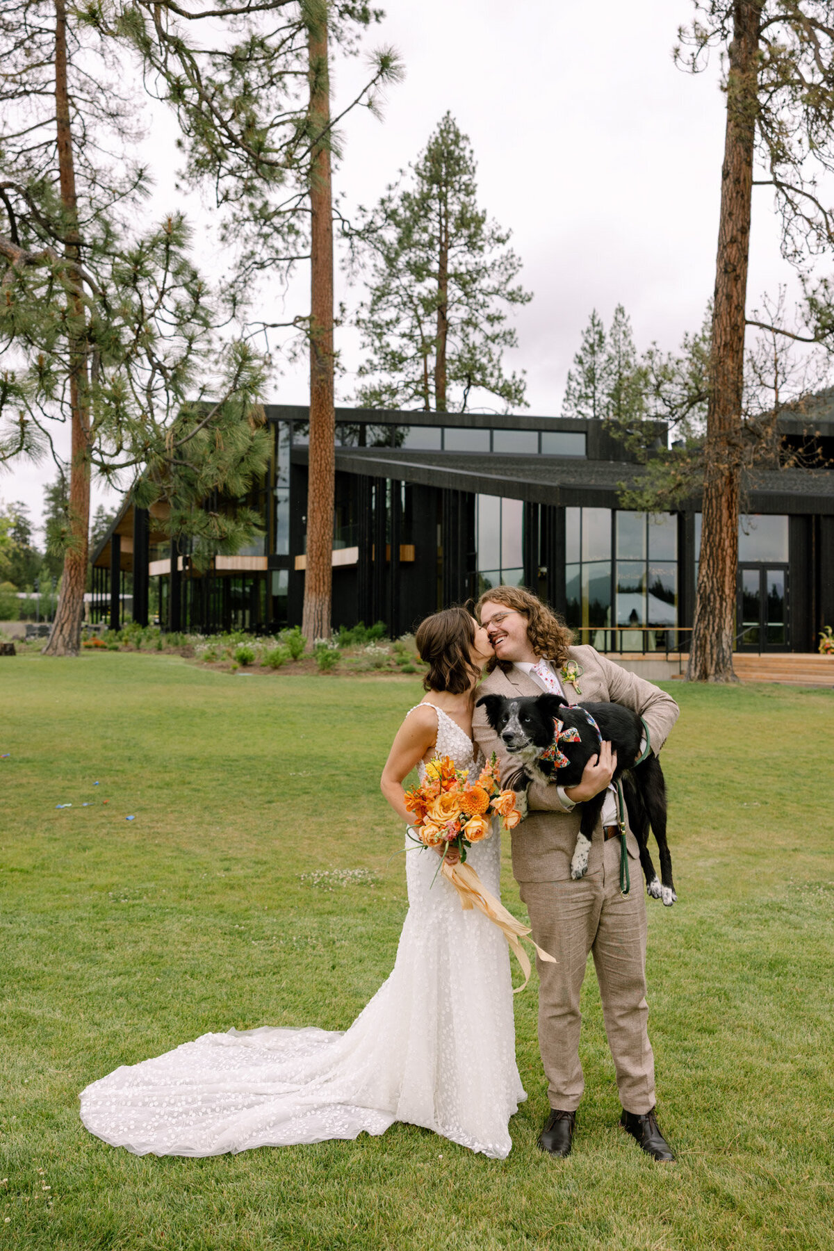 Modern oregon wedding venue in the background with a young wedding couple in front holding their pup representing full service design and calligraphy by Life in Letters.
