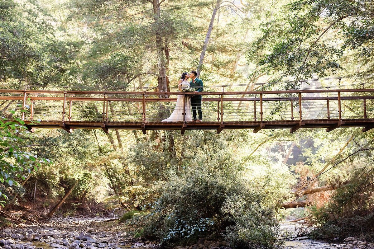 The bride and groom kiss while standing on a swing bridge in Big Sur.