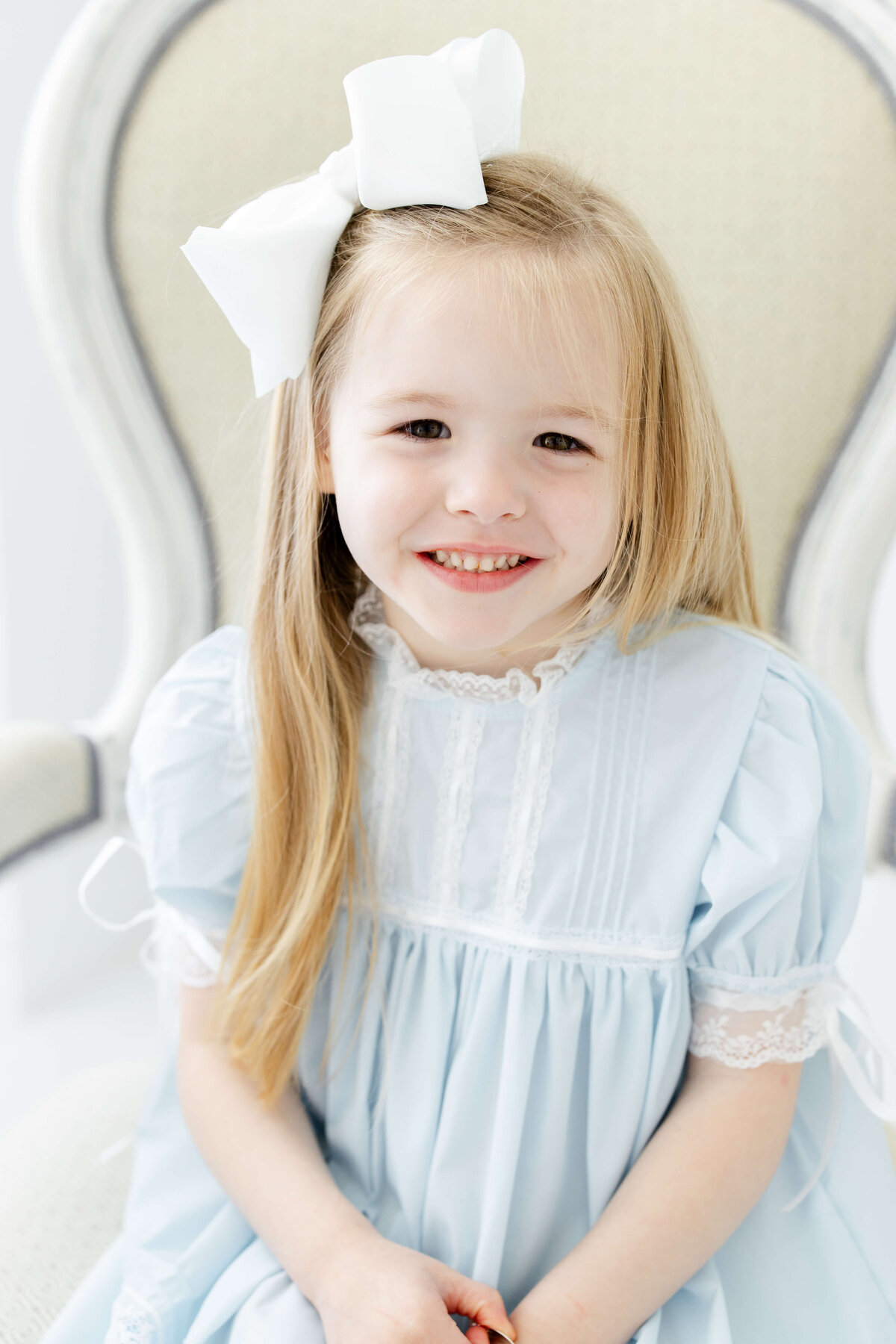 Girl sitting with bow in hair smiling at the camera in blue dress for milestone photography