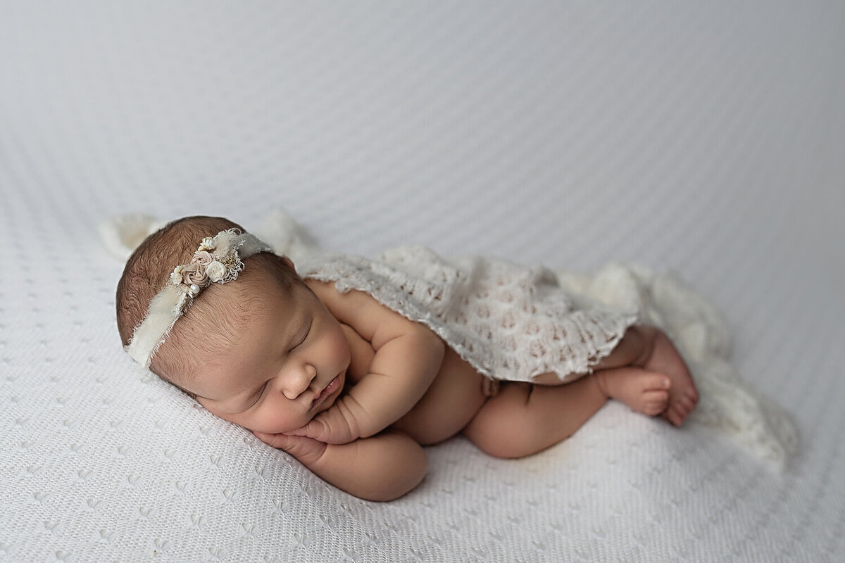 A white lace blanket covers a baby as it sleeps on a white pad