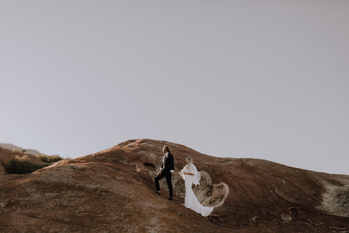 newly wed walk up red rock formation for colorado photographer