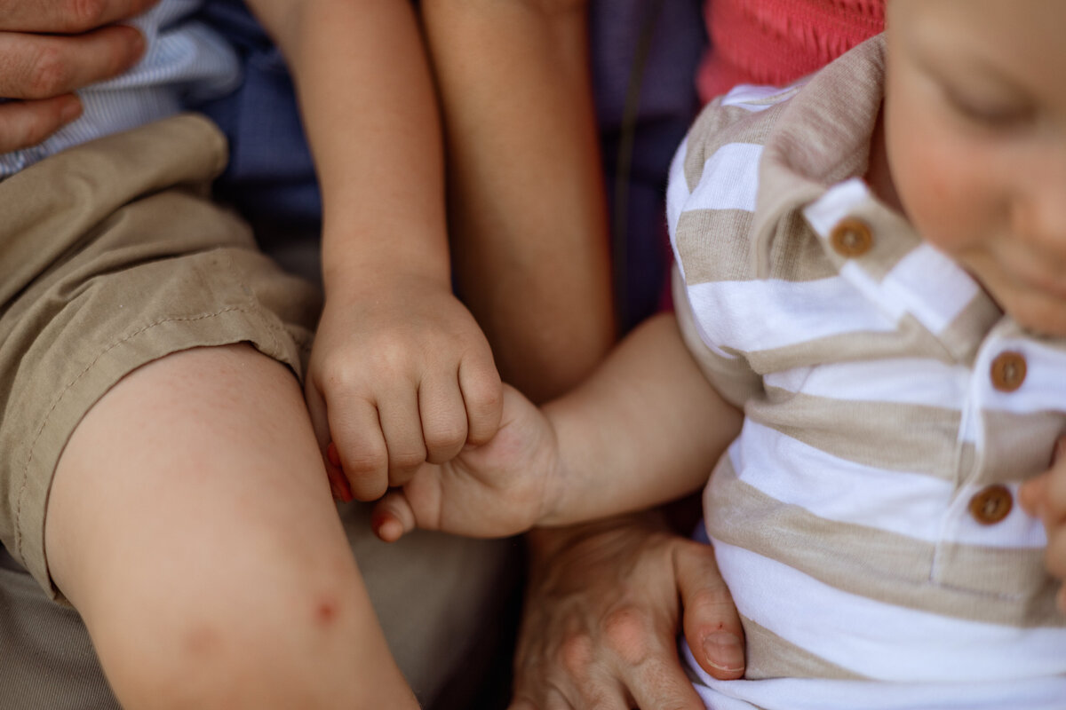 A close-up of two young siblings holding hands during a West Michigan family photography session, highlighting the sweet details of their connection and bond.