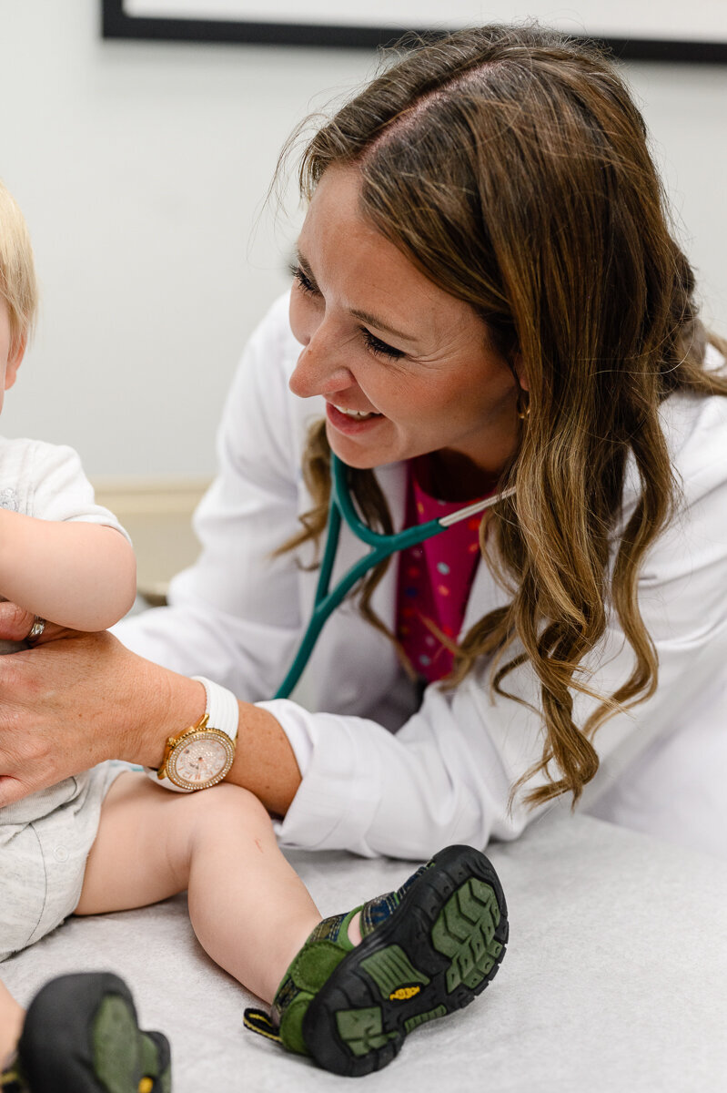 A commercial photographer and branding photographer takes a picture of a doctor examining a baby boy while smiling during a branding photography session and branding photos and brand pictures.