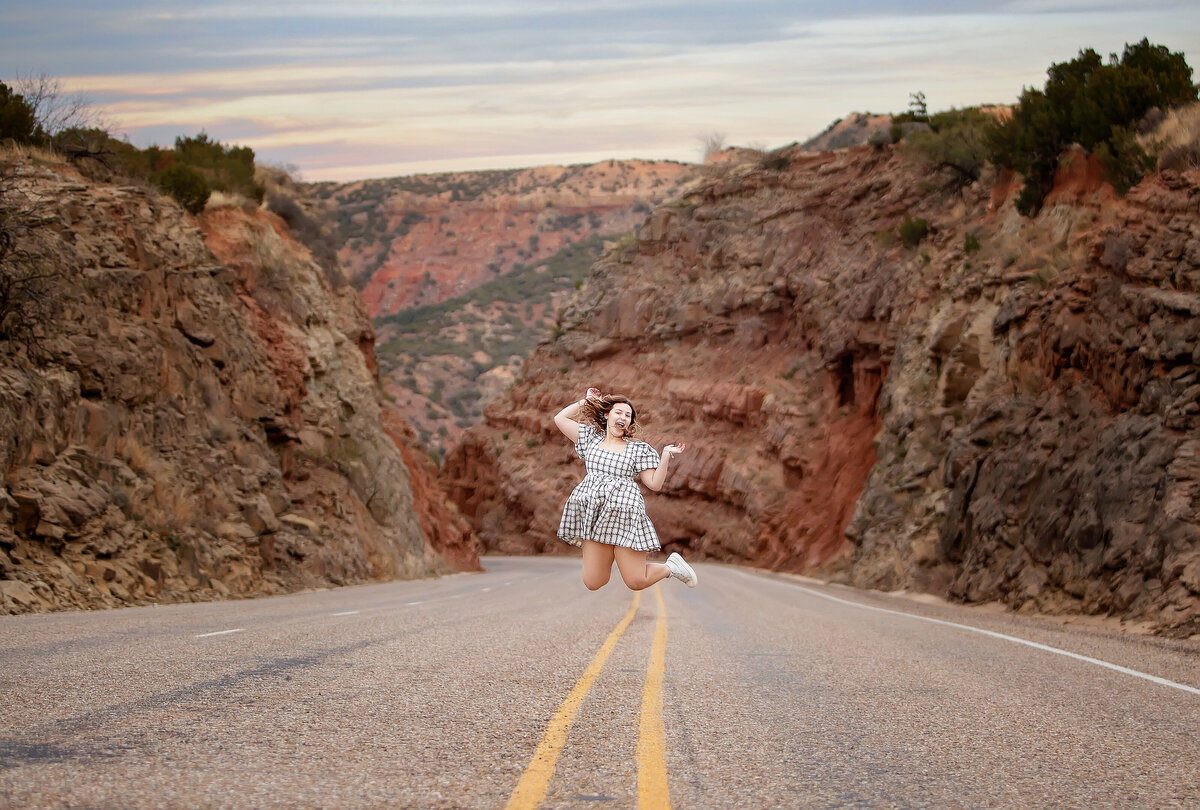 Senior girl jumping at Claudes Crossing canyons in middle of road