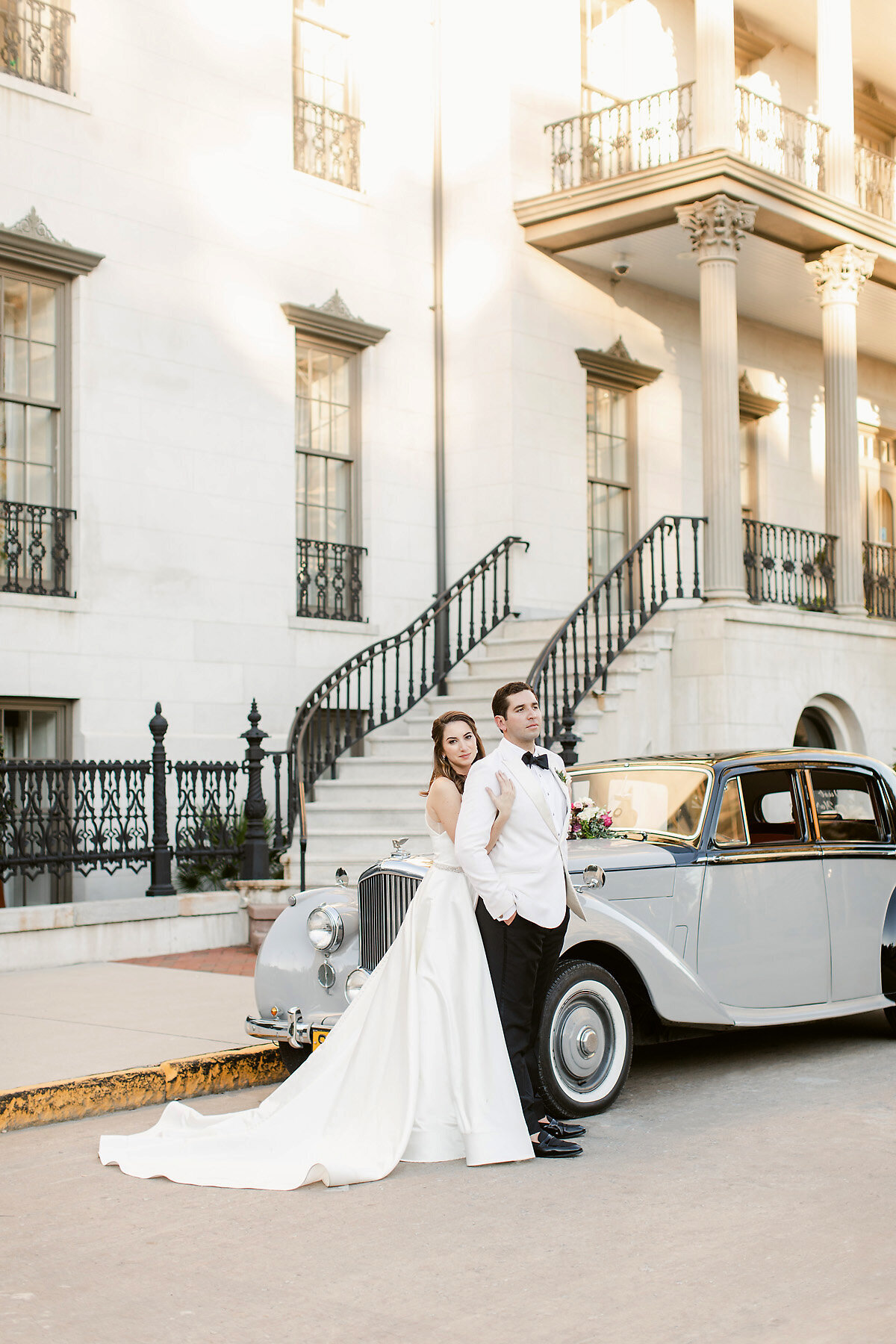 Bride and groom sanding in front of rolls royse.