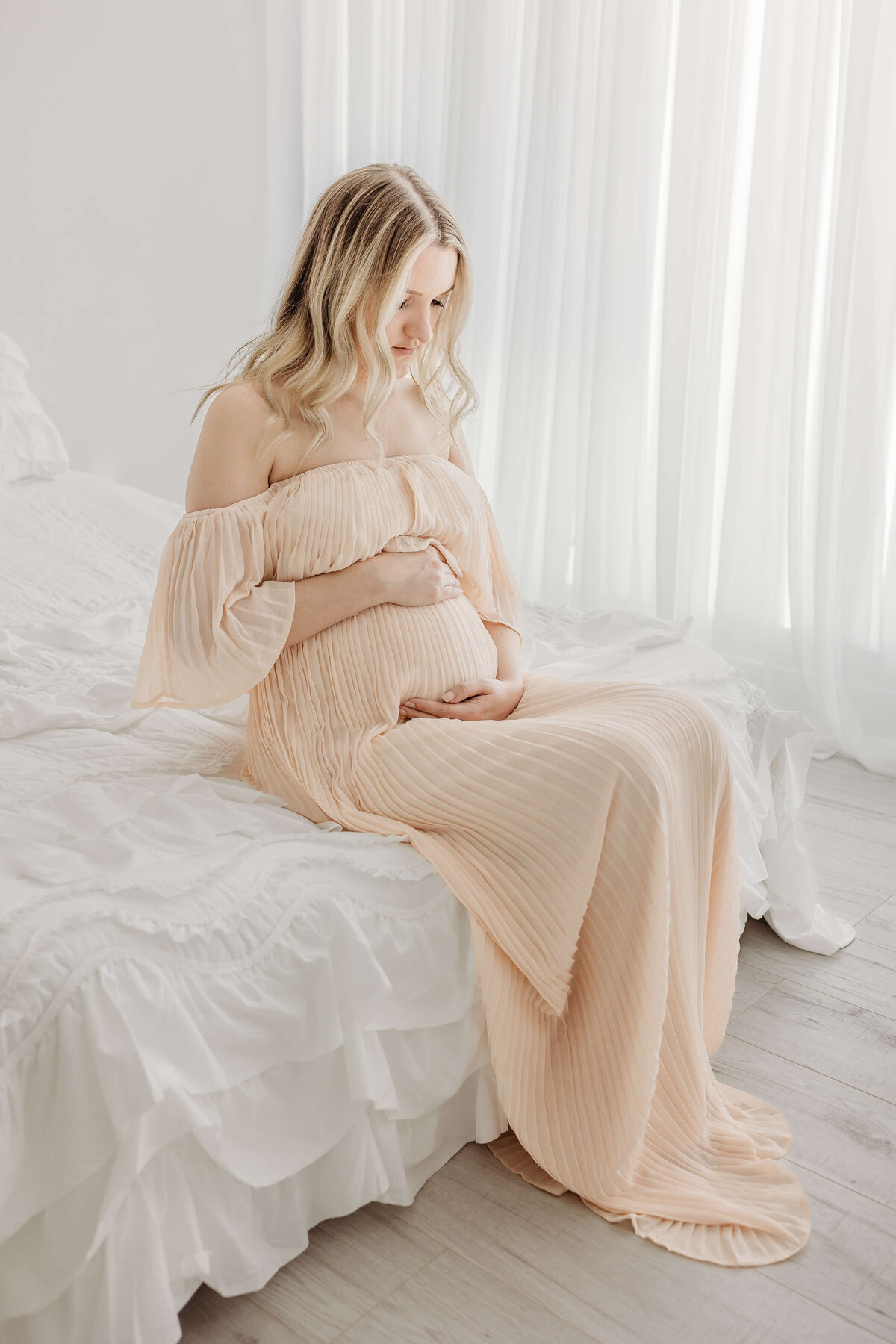 Woman sitting on white bed and pregnant for photoshoot