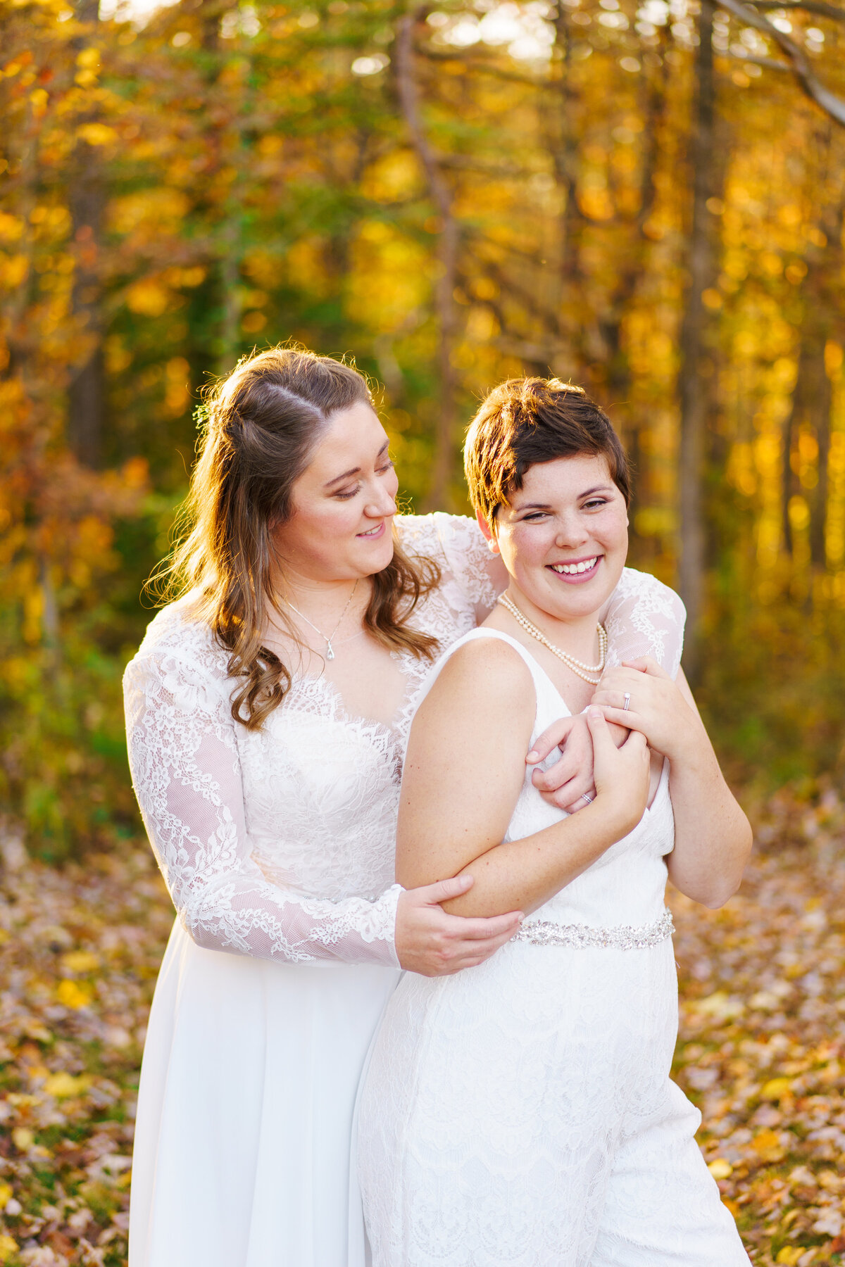 Bride holds her bride as they smile in front of  colorful fall leaves at their wedding at the Grove at Cedar Falls in Hocking Hills,.