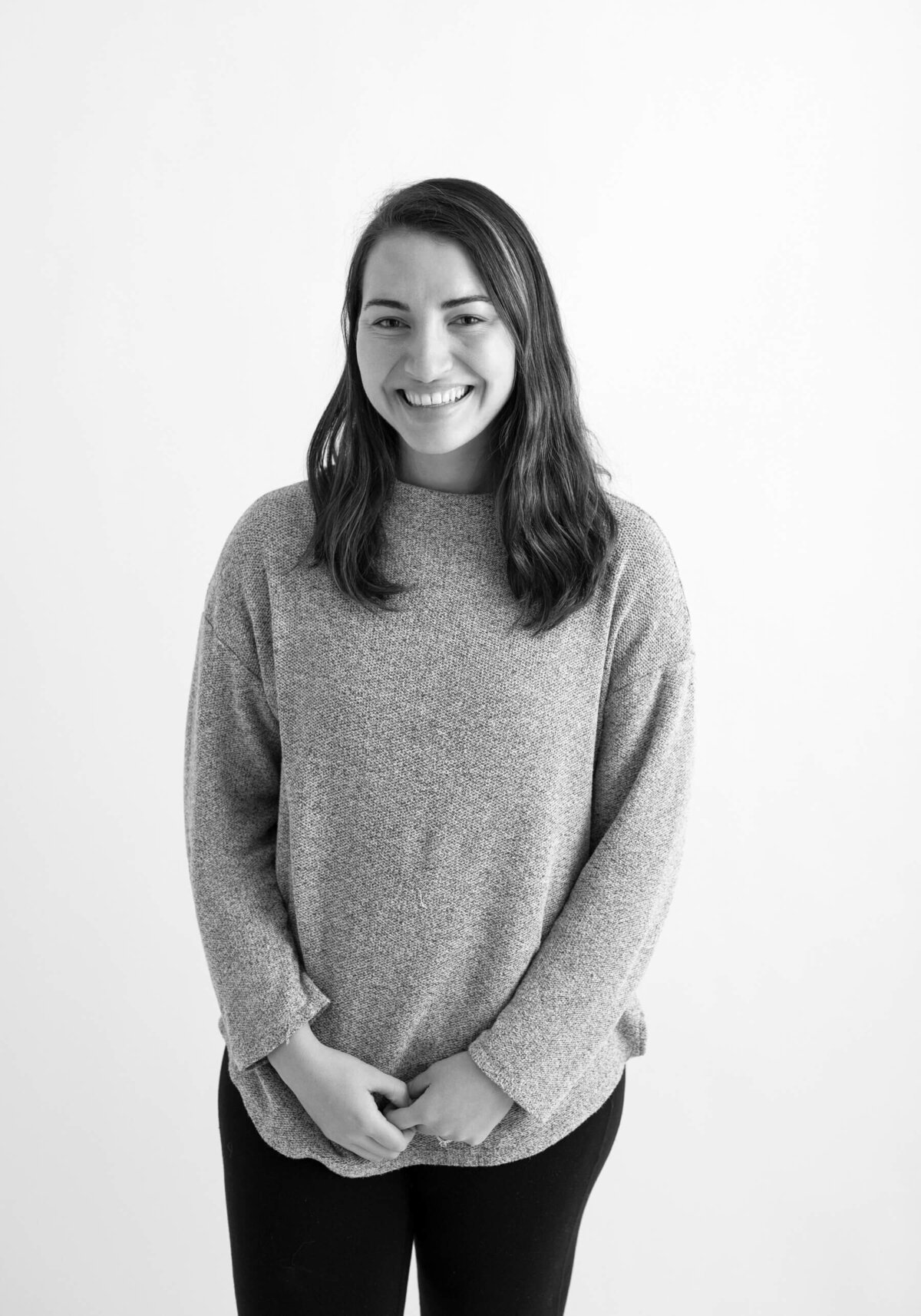 Black and white before shot of a woman in a sweater, smiling naturally against a plain white background. Studio before shot o