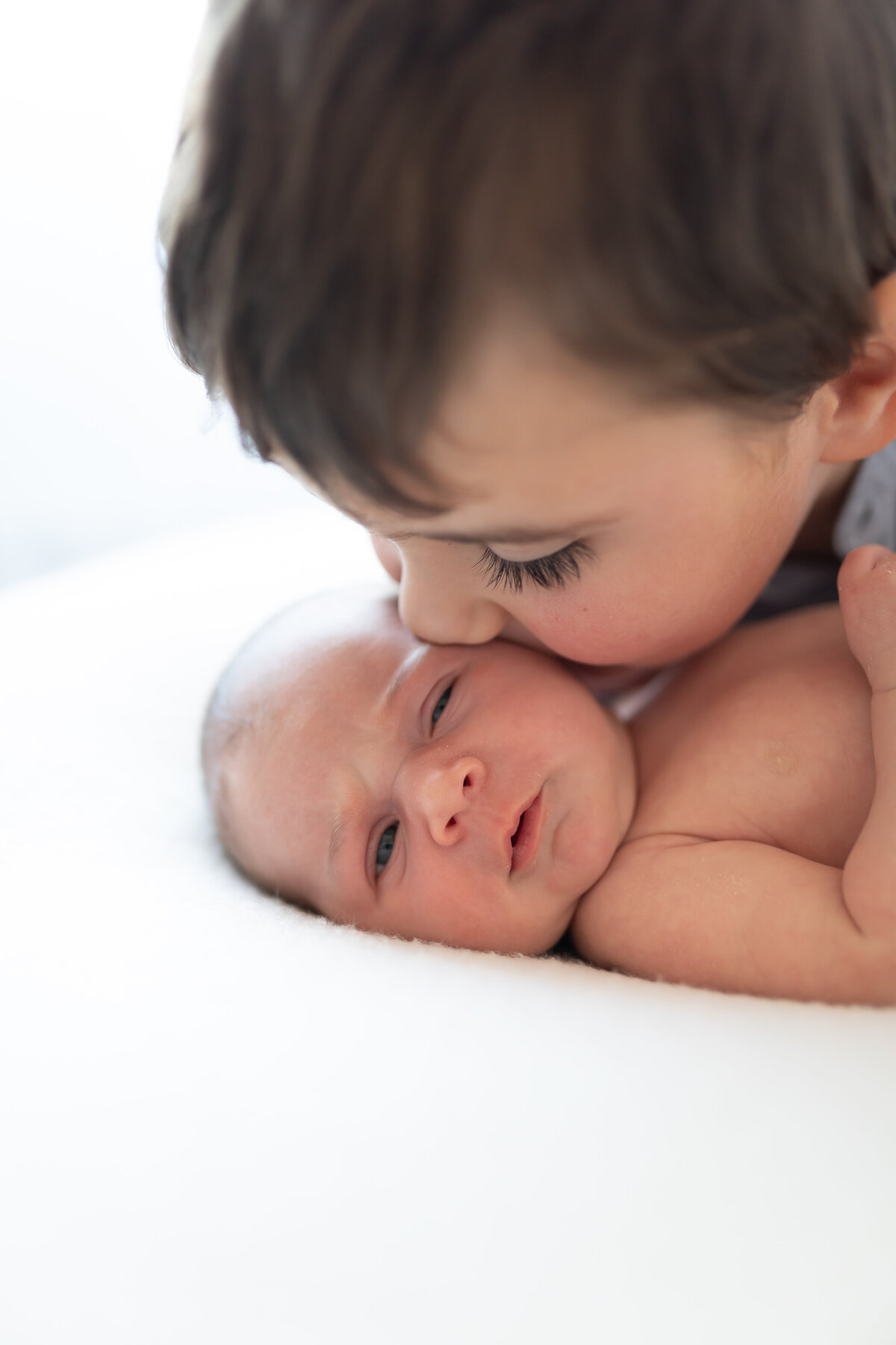 older sibling kissing newborn baby sister