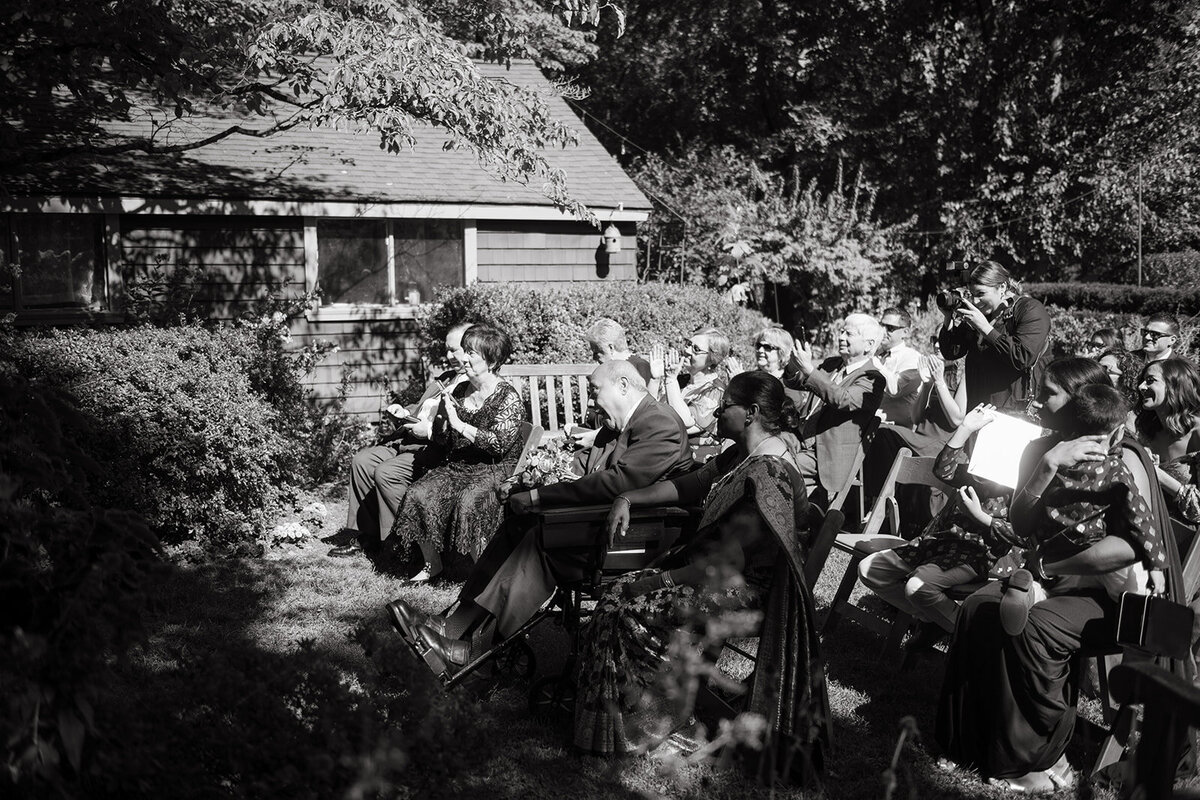 A black-and-white candid moment of guests enjoying live music in a cozy outdoor gathering space.
