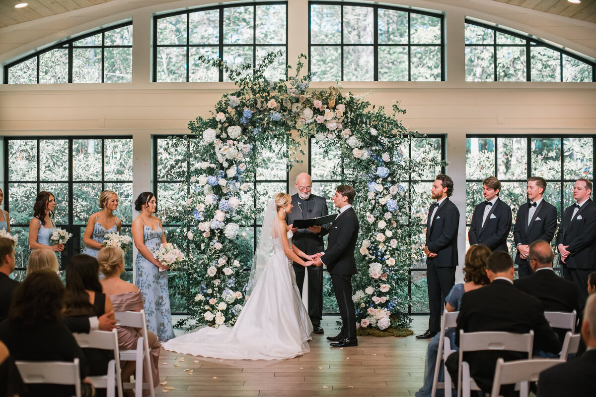 Bride and groom exchanging vows in front of a large floral arch during an indoor ceremony at Old Edwards Inn in Highlands, North Carolina.
