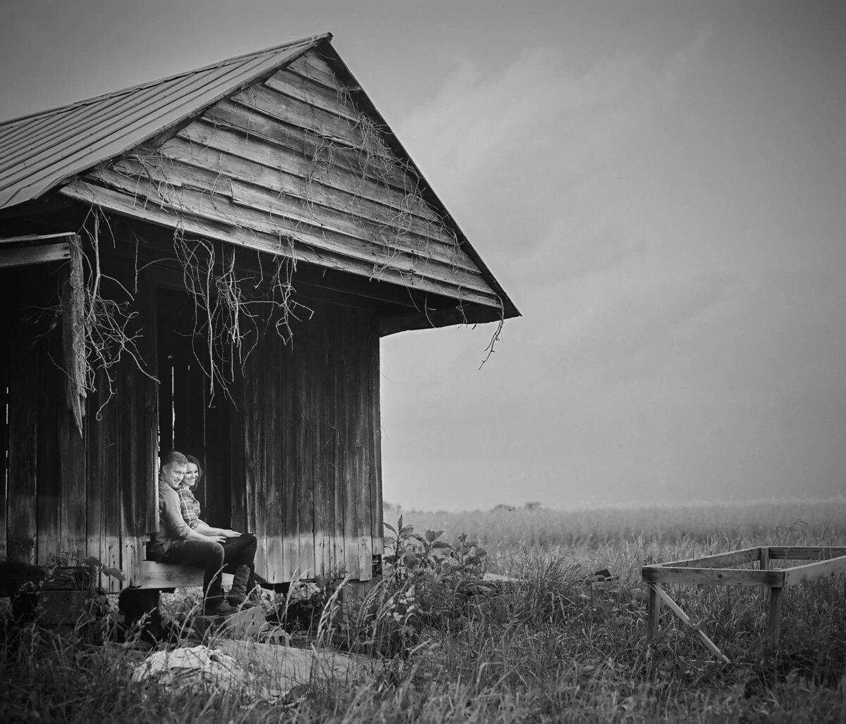 Monochrome image of a woman sitting thoughtfully in a rustic shack on a vast field