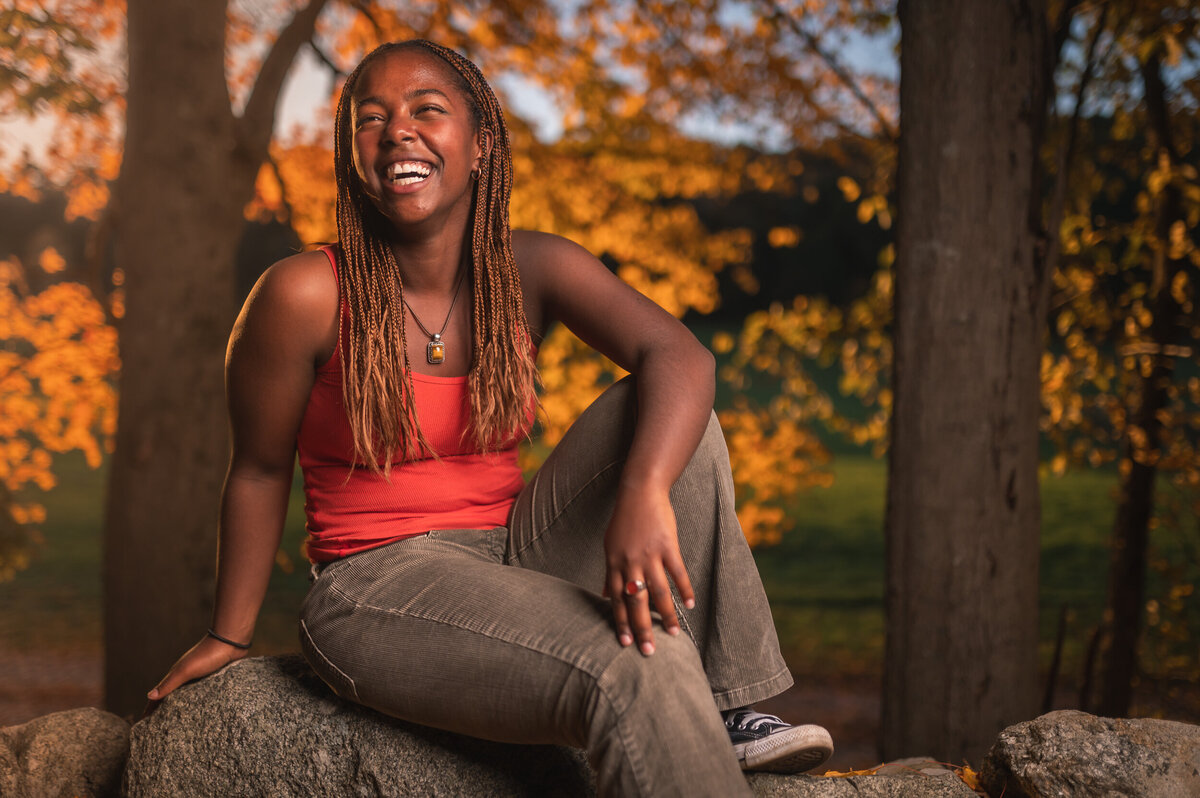 Senior portrait of black girl laughing sitting on stone wall