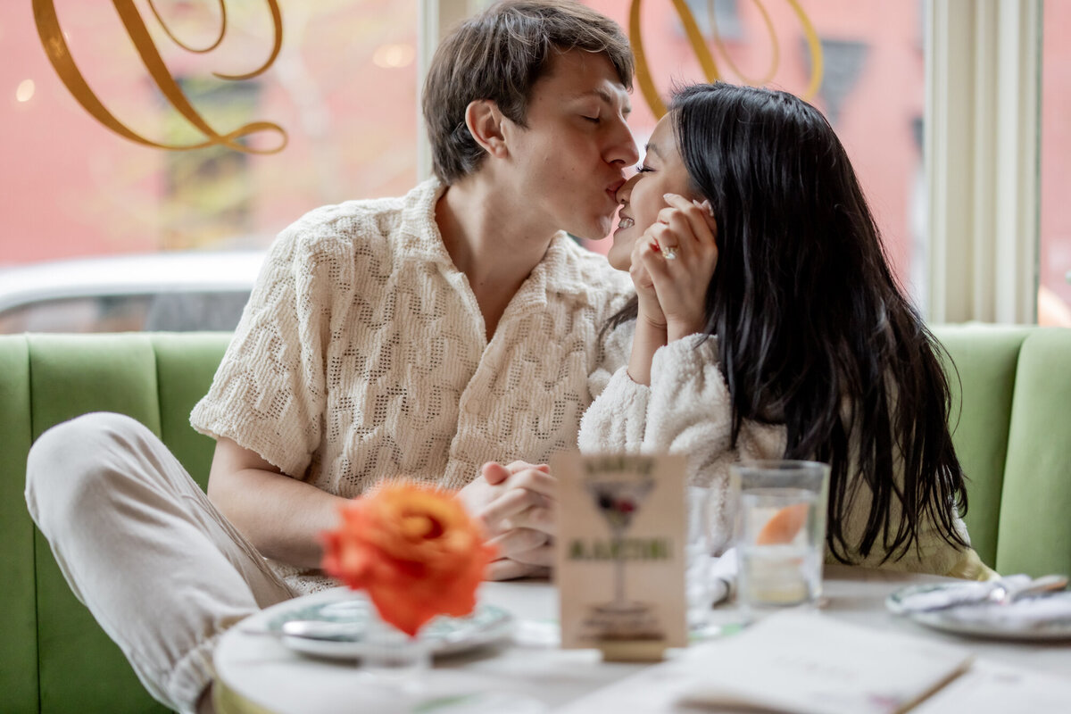 Candid moment of a couple sharing a forehead kiss inside a cozy West Village café during their NYC engagement session, captured by Michelle Jackson Studio.