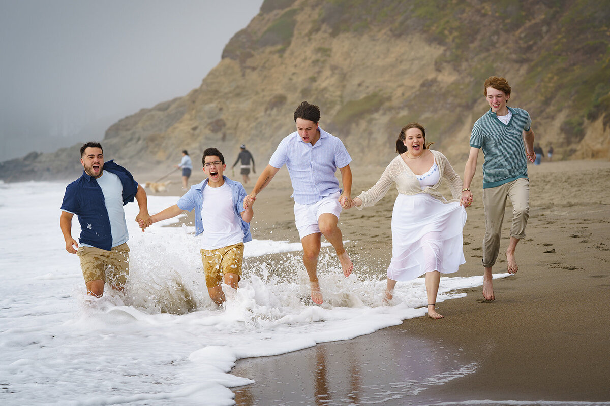 family of five kids holding hands while running down the beach in heavy surf