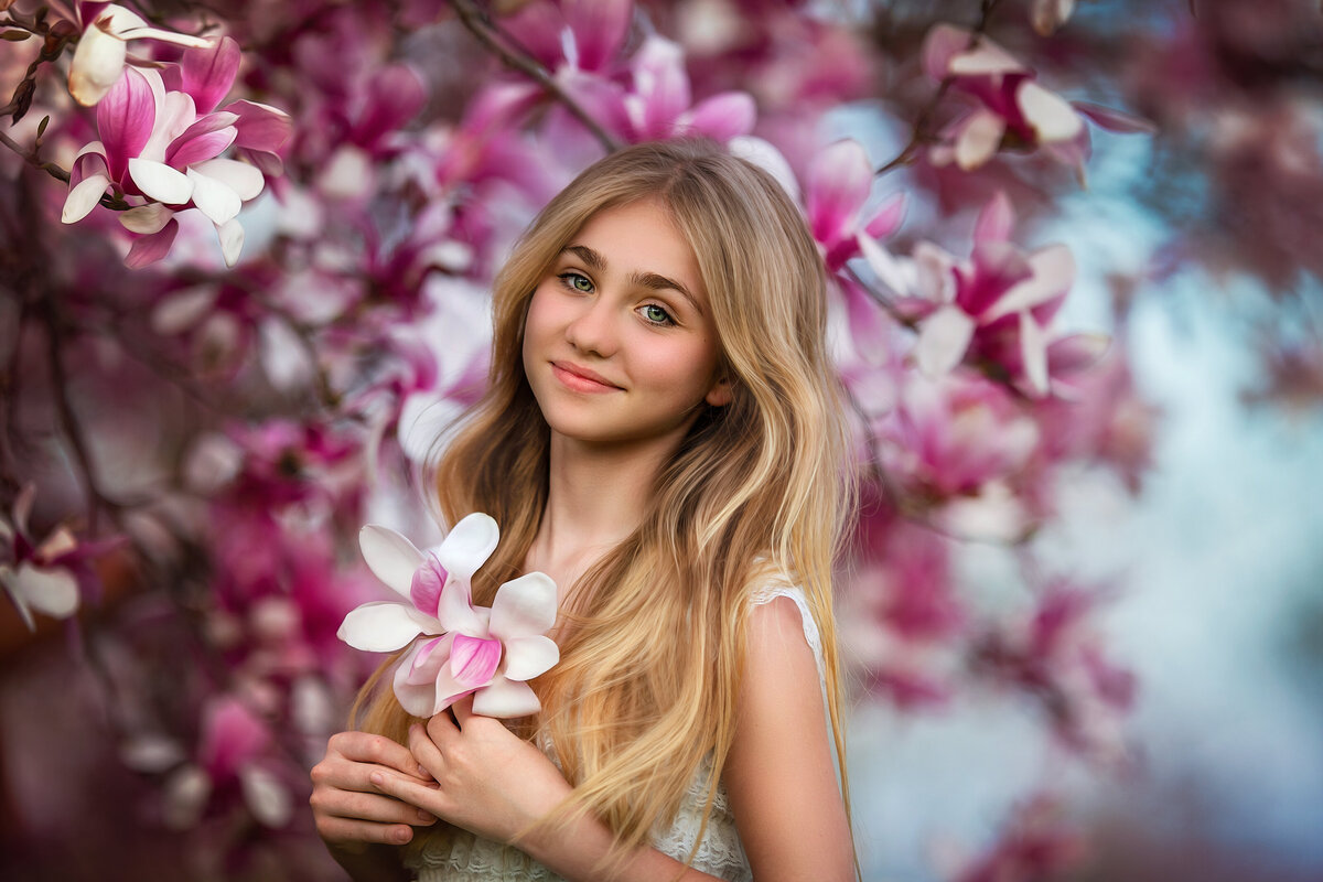 Blong girl portrait with Blooming pink magnolia blossoms in the spring,