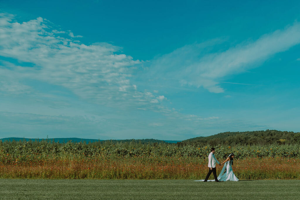 a woman and a man hold hands in wedding attire while standing in a field during the day - photo by Kay Dargen Photography