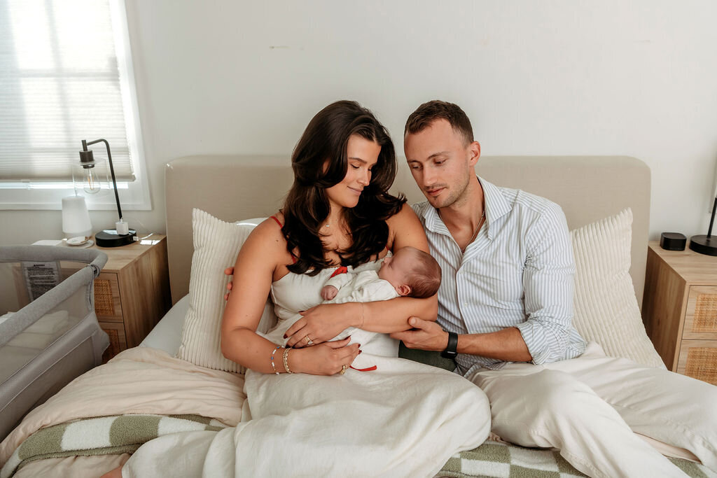 Professional Connecticut newborn photographer creates intimate lifestyle portrait of new parents admiring their newborn baby on white bed