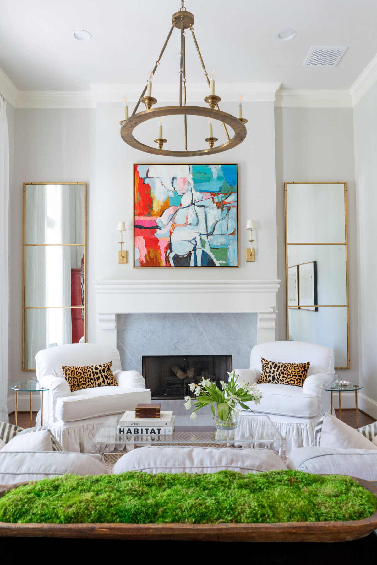 abstract art over fireplace mantle in living room with white chairs with leopard print pillows