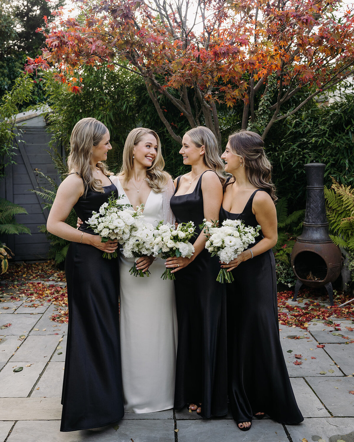 Bride smiling at her bridesmaids in black dresses while holding wedding bouquets