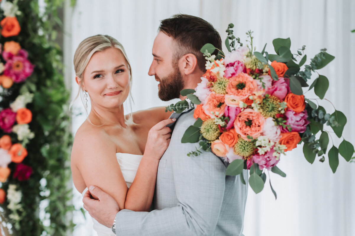 Elegant wedding portrait with coral and pink floral bouquet against white backdrop.