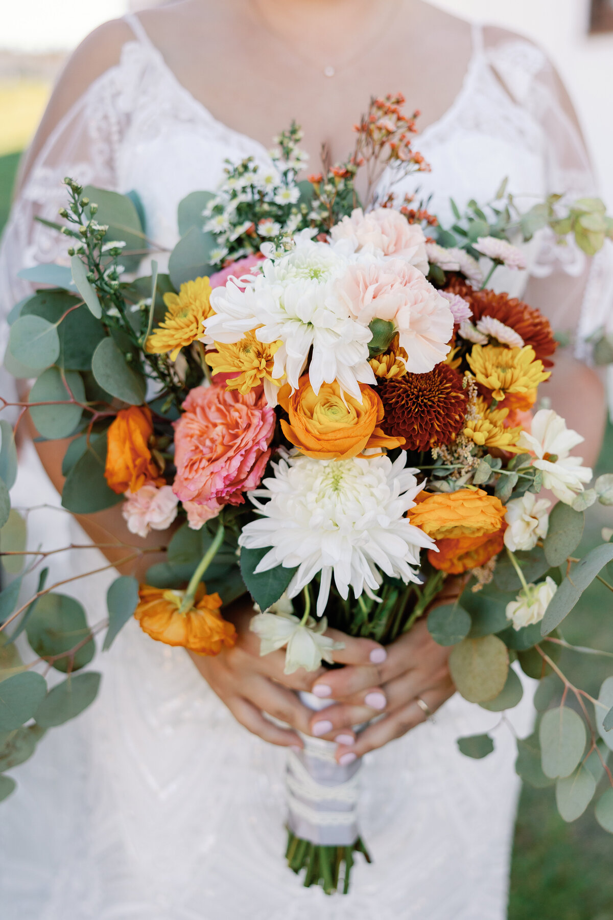 Close-up of fall wedding bouquet with white dahlias, rust roses, eucalyptus greenery, and mustard yellow accents.