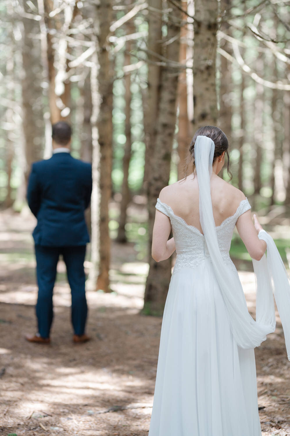 Vue de dos des mariés s’apprêtant à vivre leur first look dans une forêt de conifères des Laurentides, moment intime et chargé d’émotion capturé dans un cadre naturel et paisible