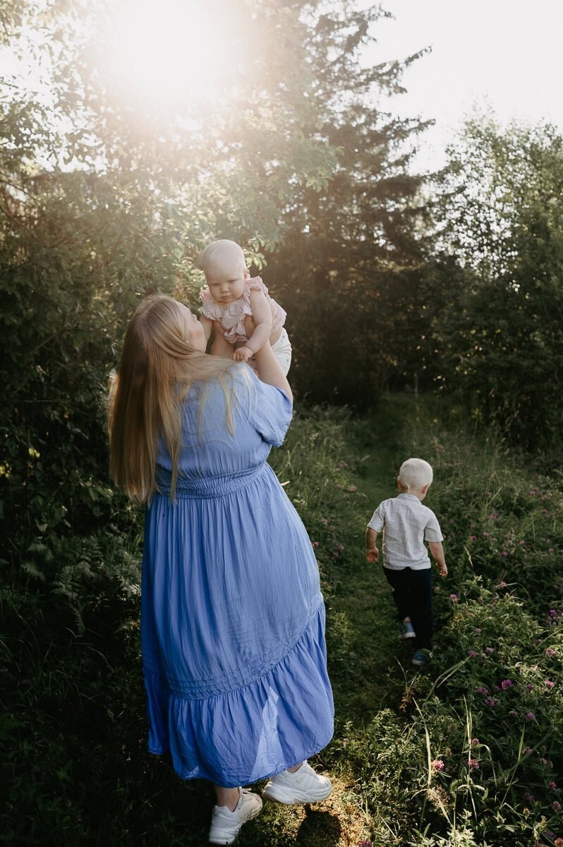 Mamma och lillasyster snurrar i solnedgång, storebror springer runt dem.