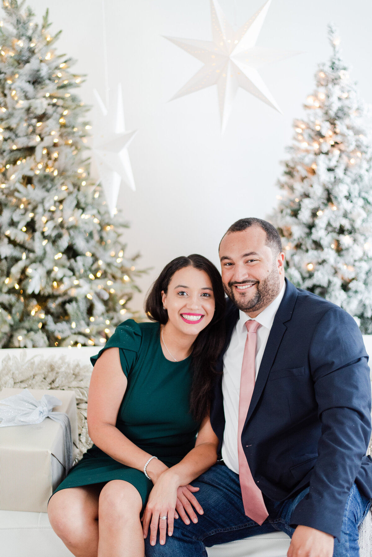 couple sitting on a white couch in front of Christmas trees